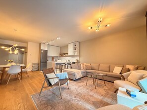 A modern living room with a sofa, coffee table, and a dining area with chairs and a table. - Cozy Forrest-side 2BR - Parking & Patio (Brașov)