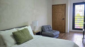 A bedroom with a bed, a chair, a nightstand, a lamp, and a door. - New centrally located apartment with balcony. (Chihuahua)
