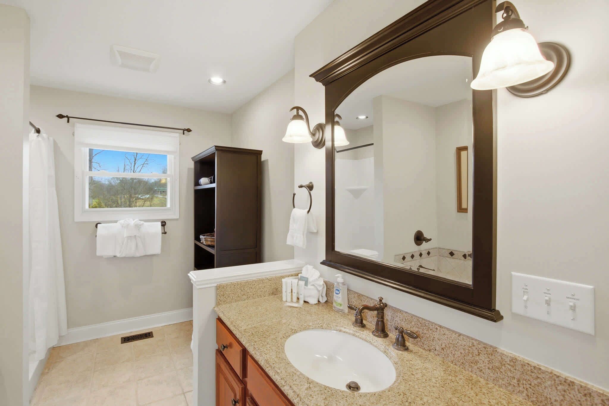 A bathroom with a large mirror, a sink, and a window.