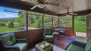 Eine überdachte Terrasse im Freien mit Korbmöbeln, einem Deckenventilator und Blick auf eine grüne Landschaft.