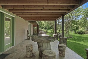 Un espace extérieur abrité, doté d’un banc en pierre, de poutres en bois et d’un chemin en pierre menant à l’entrée d’un bâtiment.