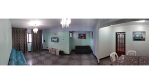Una habitación con sofá, televisor, una mesita y un comedor con sillas.