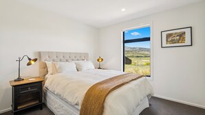 Un dormitorio con una cama grande, una mesita de noche con lámpara, una ventana con vistas al paisaje y un cuadro en la pared.