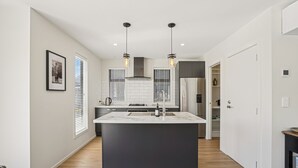 Una cocina moderna con una isla central, luces colgantes y vistas al salón contiguo.