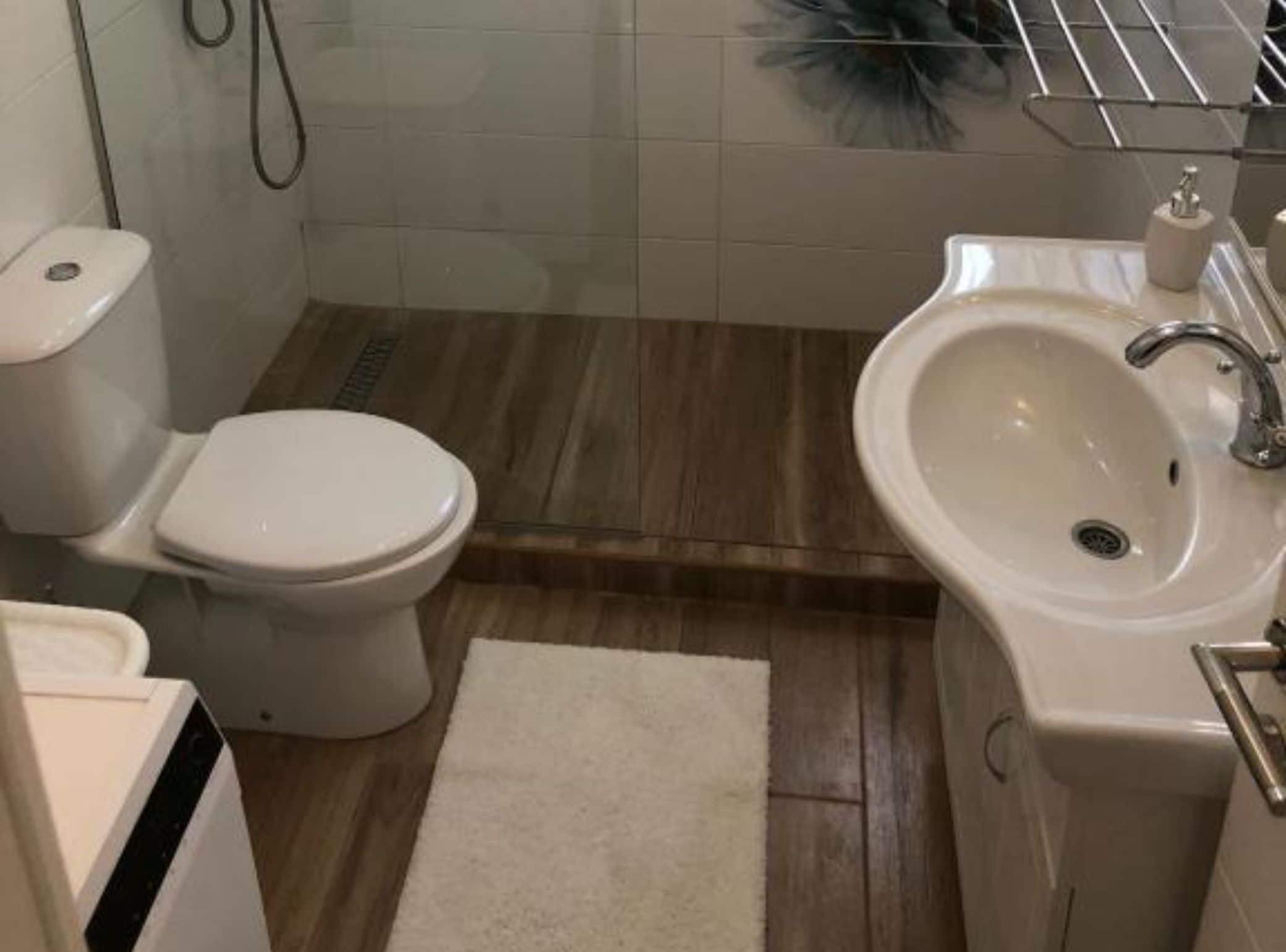 A bathroom with a toilet, sink, and wooden flooring.