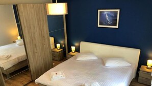 Ein ordentlich bezogenes Bett mit weißen Leinen, zwei Nachttische mit Lampen, ein gerahmtes Bild an der Wand und ein Holzboden.