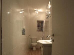 A small, modern bathroom with white tiles, a toilet, a sink, and a window.