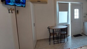 A compact living space with a kitchenette, a dining area with a small table and chairs, a television mounted on the wall, and a door leading to another room.