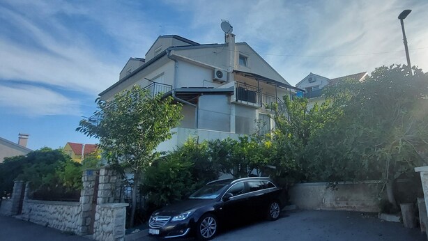 A two-story house with a balcony, a stone wall, and a parked car.