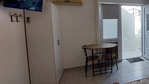 A room with a television mounted on the wall, a small table with chairs, and a sliding glass door leading to an outdoor area.