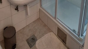 A bathroom with a white sink, a toilet, a shower, and a small trash bin.