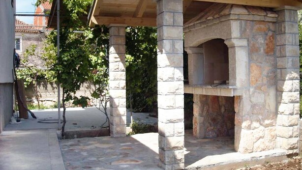 A stone-built outdoor kitchen with a chimney, surrounded by a stone wall and greenery. - Casa Dolce Mare (Pasman)