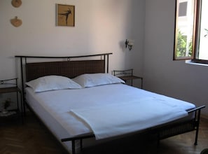 A single bed with a metal frame, white bedding, and a wooden headboard. There is a small table with a lamp on the right side of the bed. A framed picture hangs on the wall above the bed. - Casa Dolce Mare (Pasman)