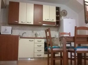 A compact kitchen with wooden cabinets, a microwave, a kettle, and a dining table with chairs.