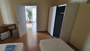 Un dormitorio con cama, armario, escritorio y una planta en maceta al fondo.