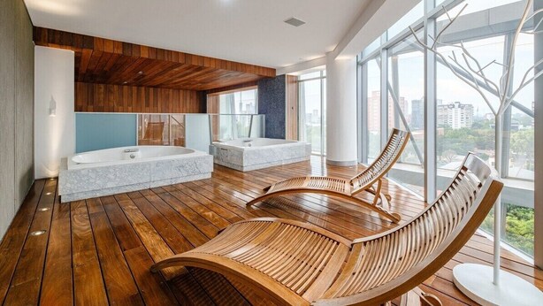 A modern bathroom with wooden flooring, a large bathtub, a freestanding shower, and a seating area with wooden loungers. - 2BR Luxury Stay Mundial 2026 Skyline Views (Mexico City)