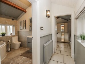 A modern bathroom with a toilet, sink, and shower. There is a radiator on the wall and a window with blinds. - The Dove Cot (Ambleside)