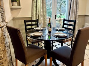 A dining table set for four with chairs, a bottle of champagne, and wine glasses. - The Dove Cot (Ambleside)