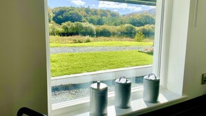 Una ventana con vista a un lago, una zona de césped y árboles.