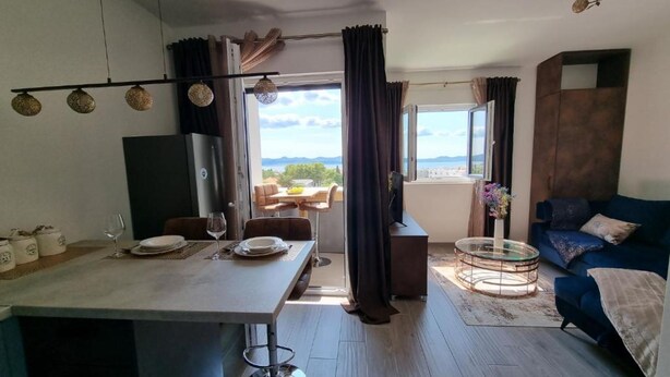 Uma sala de estar moderna com um sofá, uma área de jantar com mesa posta para dois e vista para o exterior.