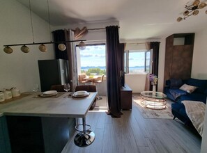 Una sala de estar moderna con un sofá, un comedor con mesa dispuesta para dos personas, y vistas al exterior.