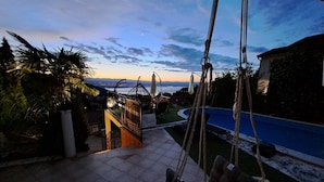 A patio with a hanging chair, a pool, and a view of the sunset over the water. - Beautiful Unique Family Villa Emily (Opatija)