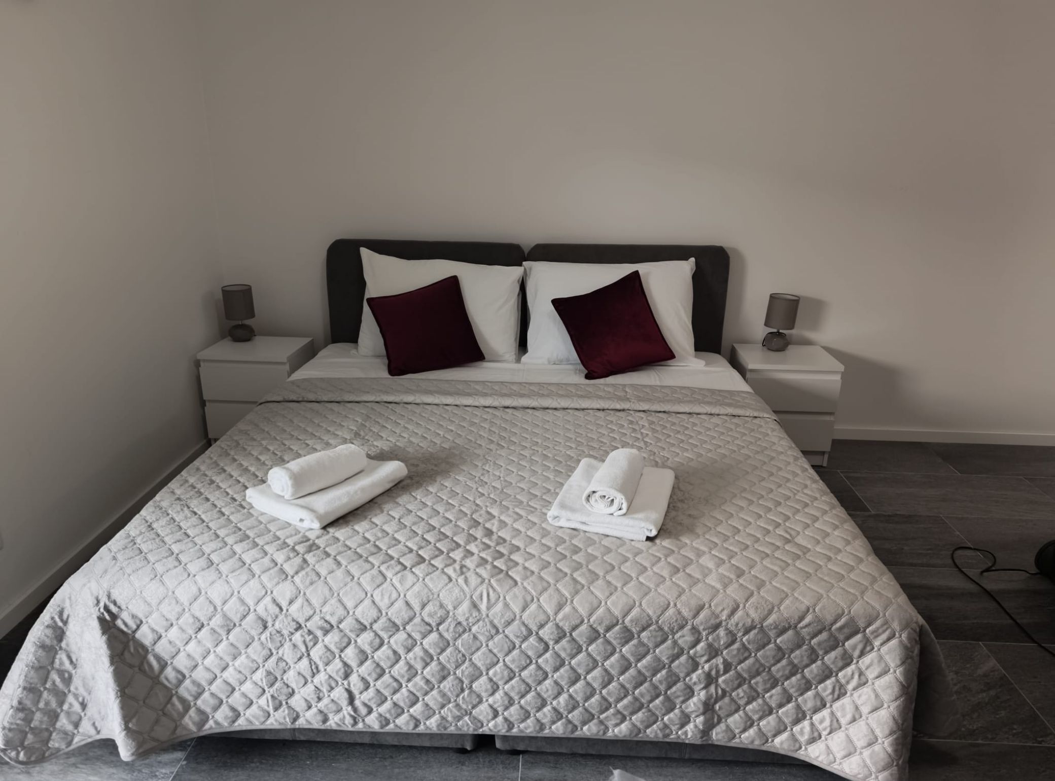 Een net opgemaakt bed met een gewatteerde sprei, twee kussens en twee opgerolde handdoeken.