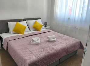 Een opgemaakt bed met een roze quilt, twee kussens en twee opgerolde handdoeken.
