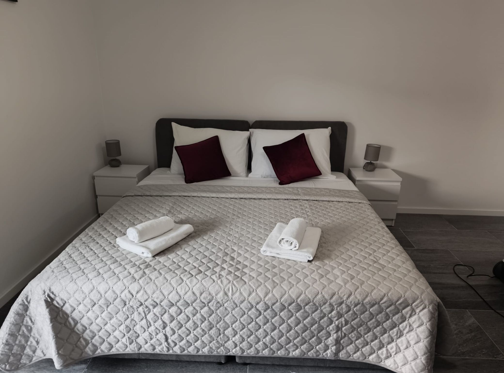 A neatly made bed with a quilted bedspread, two pillows, and two rolled towels on the bed.