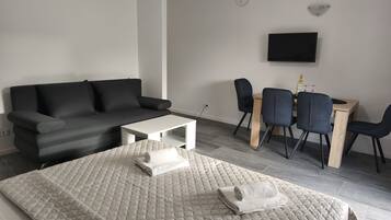 Un dormitorio moderno y minimalista con una cama grande, un sofá gris, una mesita blanca pequeña y un escritorio con dos sillas.