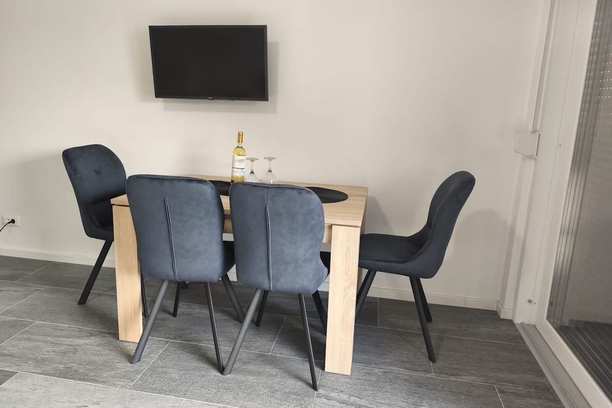 Een eetgedeelte met een houten tafel en vier stoelen, een fles wijn en een flatscreen televisie aan de muur.