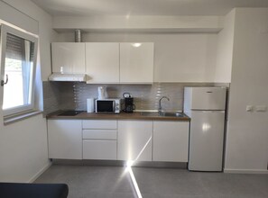 A modern kitchen with white cabinets, a stainless steel sink, a microwave, a coffee maker, and a refrigerator. - Apartments Tourist Port (Dubrovnik)