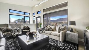 A modern living room with a large window, a sofa, a coffee table, and a TV. - The Gallery! Luxury Residence w/ Front Range Views (Monument)