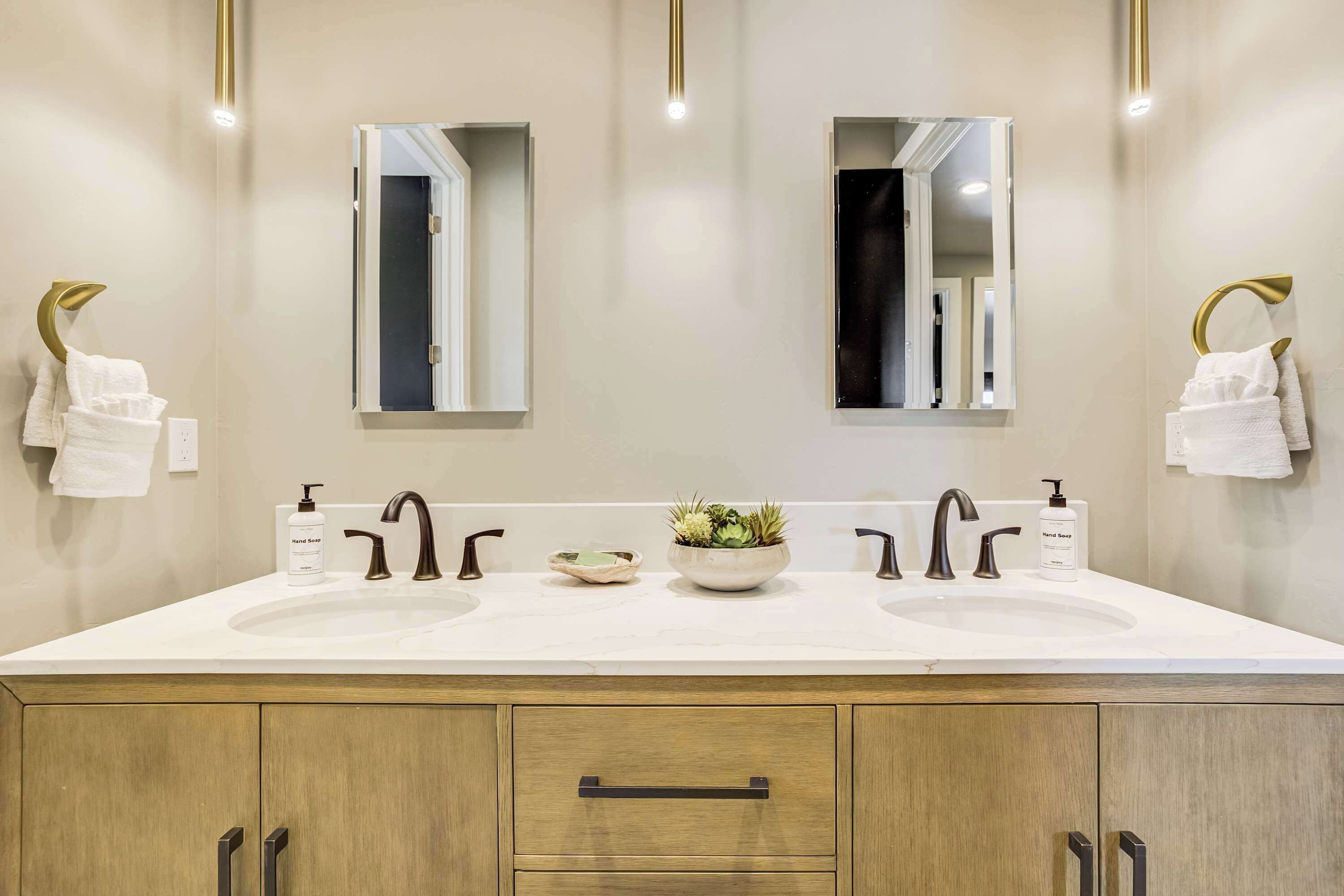 Ein modernes Badezimmer mit zwei Waschbecken, einer zentral platzierten Pflanze und goldenen Armaturen.