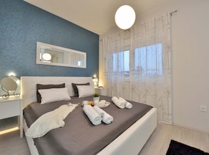 A bedroom with a bed, bedside tables, a mirror, and a window with curtains. - Villa Marija Exclusive Stay (Sukosan)