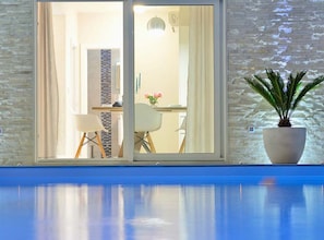 A poolside view with a sliding glass door leading to a dining area with chairs and a table. - Villa Marija Exclusive Stay (Sukosan)