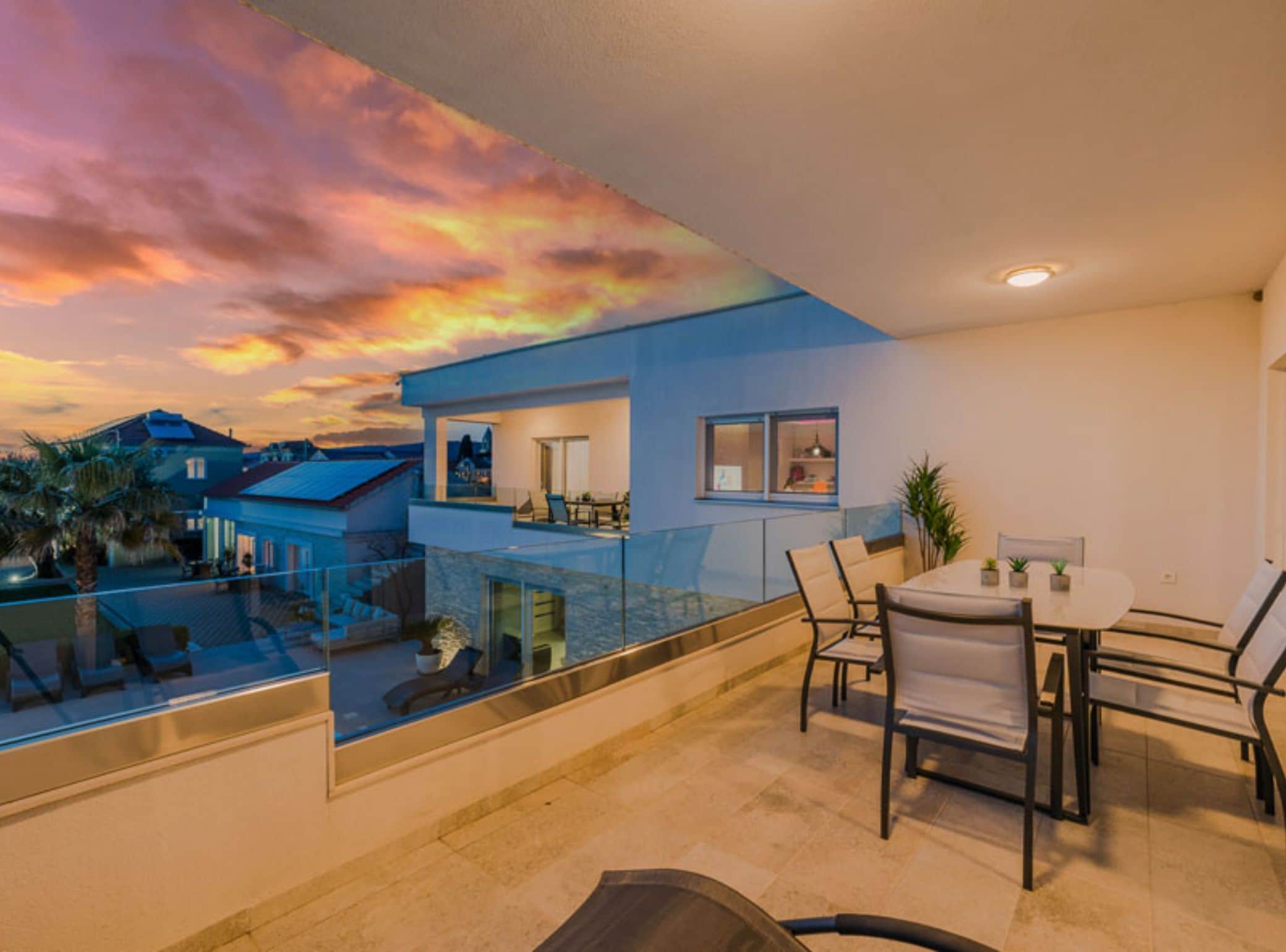 A modern apartment with a balcony, a dining area, and a view of the sunset.