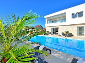 A modern two-story building with a swimming pool, lounge chairs, and a palm tree. - Villa Marija Exclusive Stay (Sukosan)