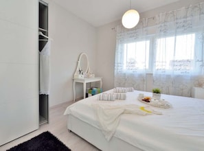 A bedroom with a bed, a vanity with a mirror, a window with curtains, and a small table with a plant. - Villa Marija Exclusive Stay (Sukosan)