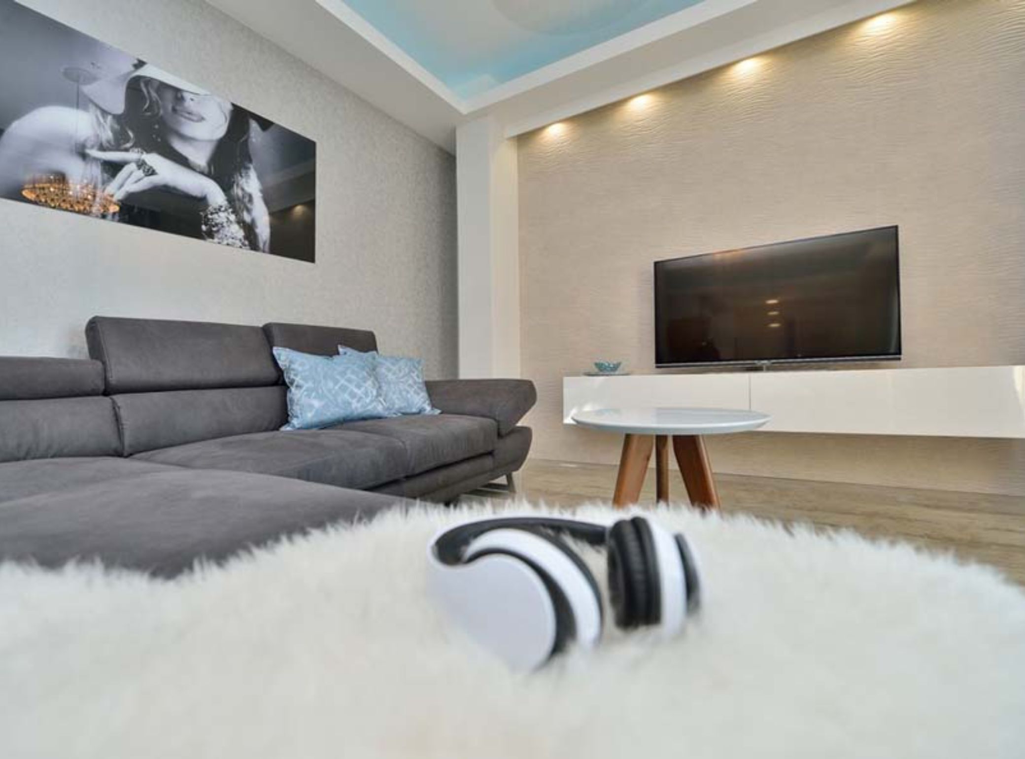 Un soggiorno moderno con un divano grigio, una TV a schermo piatto fissata al muro e un tavolino rotondo bianco.