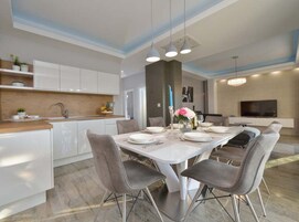 A modern kitchen with white cabinets, a wooden countertop, and a dining area with a white table and grey chairs.