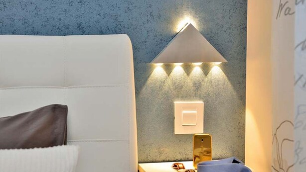 A neatly made bed with a white headboard, a bedside lamp with three light bulbs, a wall socket, and a smartphone on the nightstand. - Villa Marija Exclusive Stay (Sukosan)