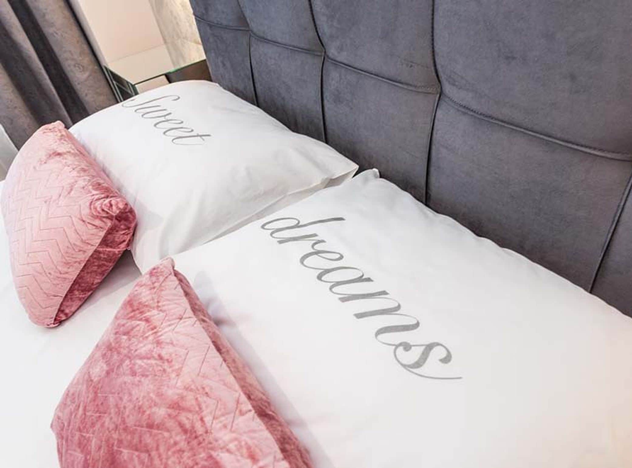 Ein Bett mit zwei Kissen, auf dem eines 'Liebe' und das andere 'Träume' aufgestickt hat.