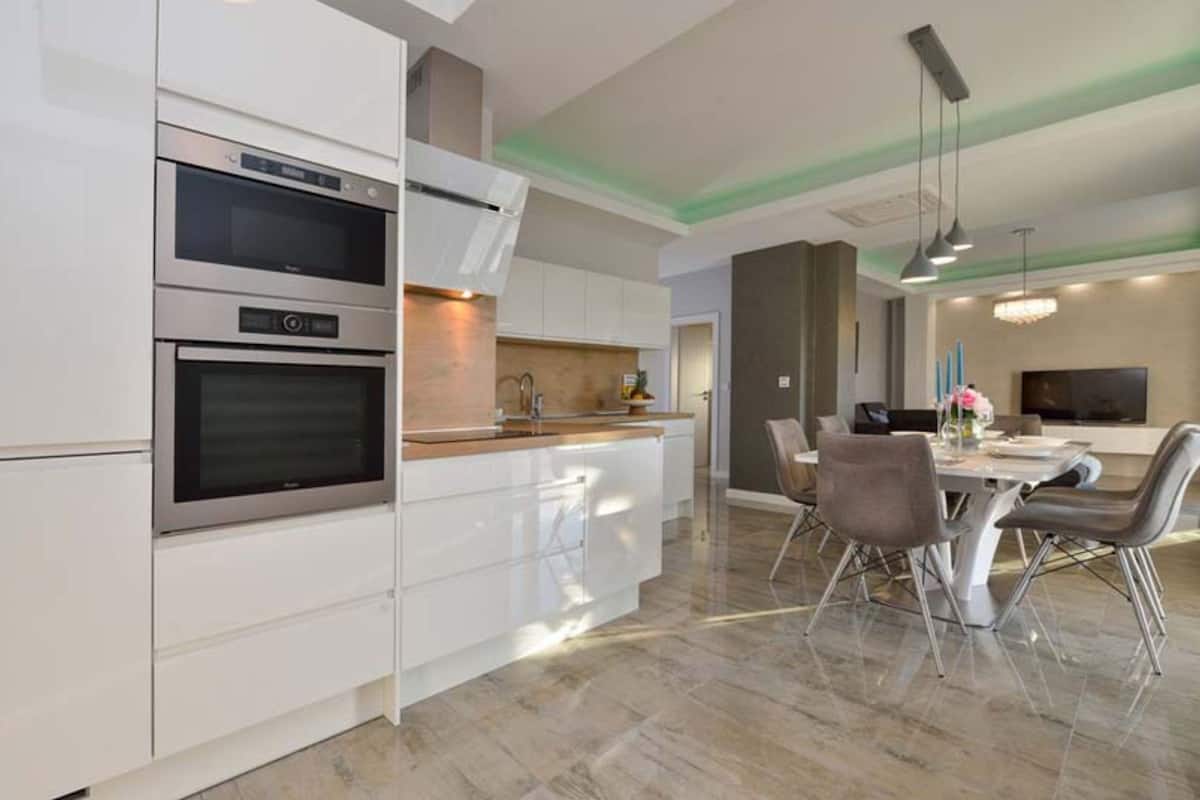 A modern kitchen with built-in appliances, a dining area with a table and chairs, and a TV mounted on the wall.