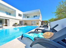 A modern two-story house with a swimming pool, outdoor seating, and a clear blue sky.