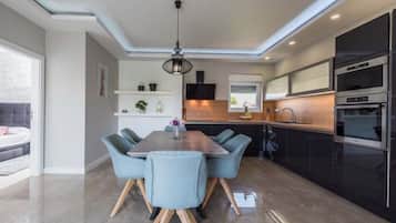 A modern kitchen with built-in appliances, a dining area with a wooden table and blue chairs, and a large window providing natural light.