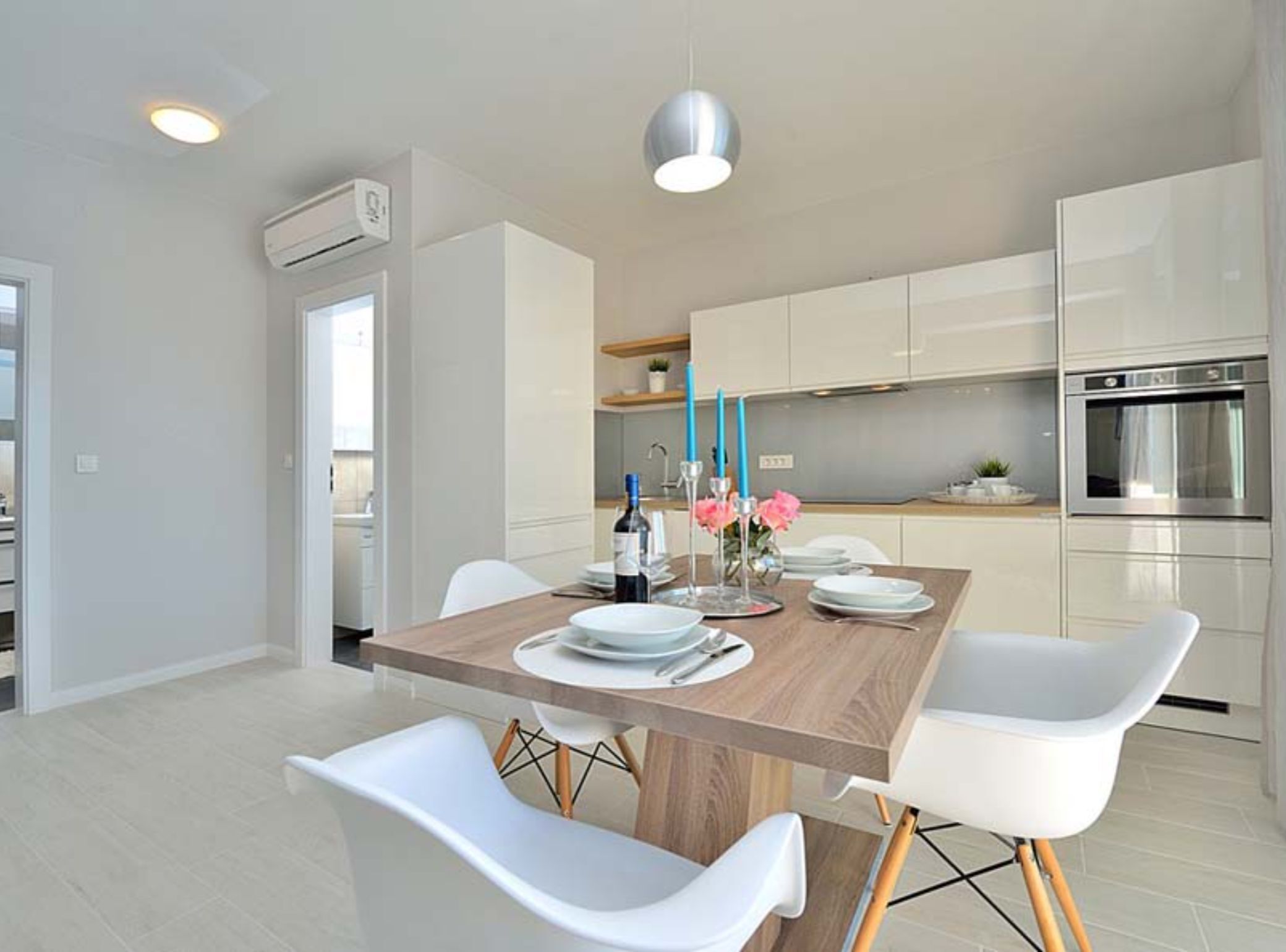 A modern kitchen with white cabinetry, a wooden dining table, and white chairs.