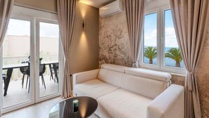 Een moderne woonkamer met een witte bank, een glazen salontafel en uitzicht op zee door grote ramen.