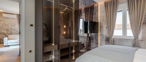 Een moderne slaapkamer met een groot bed, een inloopkast met glazen deuren en een uitzicht naar buiten door een raam.