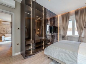 Une chambre moderne avec un grand lit, un dressing avec des portes en verre et une vue sur l’extérieur par une fenêtre.